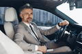 Confident man looking at camera and smiling while sitting on the front seat of a car - PhotoDune Item for Sale