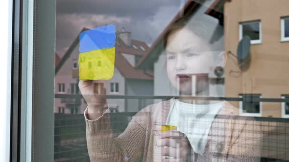 Little Girl Draws the Flag of Ukraine on the Window