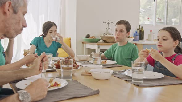 Three kids having breakfast of pancakes and fruits with their parents