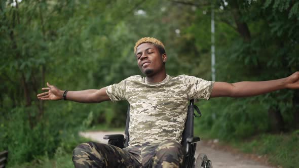 Happy Man in Wheelchair Stretching Hands with Closed Eyes Enjoying Tranquility in Forest