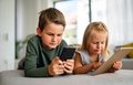 Little girl and boy watching video or playing games on their digital device tablet, smartphone - PhotoDune Item for Sale