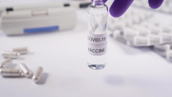 hand sets an ampoule with a coronavirus vaccine on a white table with medical equipment