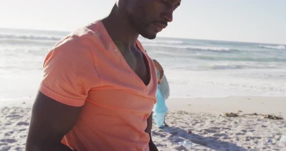 Portrait of african american couple segregating waste with gloves on sunny beach