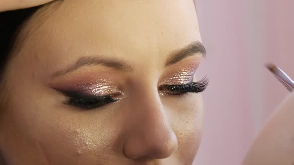 A Professional Makeup Artist Applies Shiny Bodily Eyeshadow with a Special Brush in a Makeup Studio