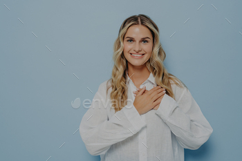 d with hands resting on her chest, standing relaxed and smiling, being grateful to whoever helped her, isolated in front of light blue background