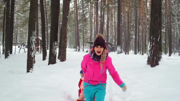Happy Woman Runs Along Snowy Park Path and Carries Sled with Kid