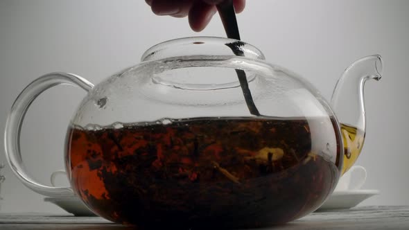 Stirring Tea in a Transparent Teapot with Spoon