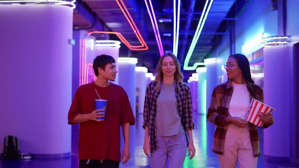 Group of Three Friends Walking By Cinema Hall with Neon Interior with Drink and Popcorn Bucket