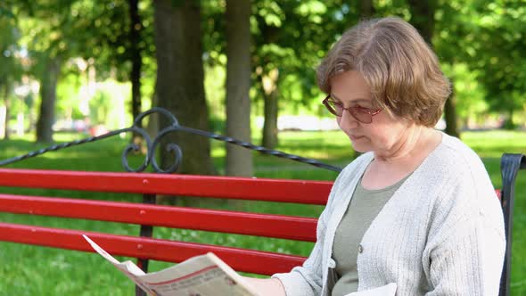 Senior Woman in Glasses Reading Newspaper in Park