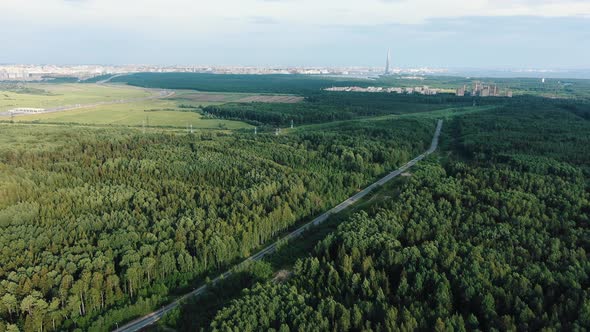 Road Stretching Among Green Forests Against City on Horizon