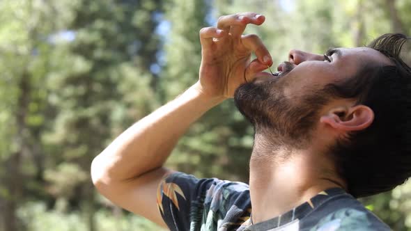 Slow Motion Shot of a man popping a cherry in his mouth and chewing on it.