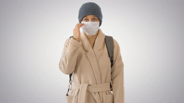 Girl in a Medical Face Mask Standing in a Coat on Gradient Background