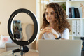 Young curly female blogger recording video at table at home - PhotoDune Item for Sale