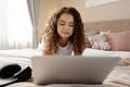 Portrait of a young curly woman using laptop in bed at home - PhotoDune Item for Sale