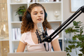 Young curly female recording podcast from home and talking into a microphone - PhotoDune Item for Sale