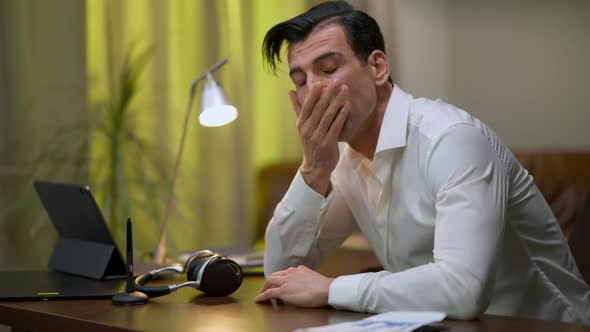 Troubled Middle Eastern Young Man Rubbing Face Thinking Sitting at Table in Home Office