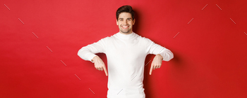 Image of smiling handsome man in white sweater inviting visit page, pointing fingers down and
