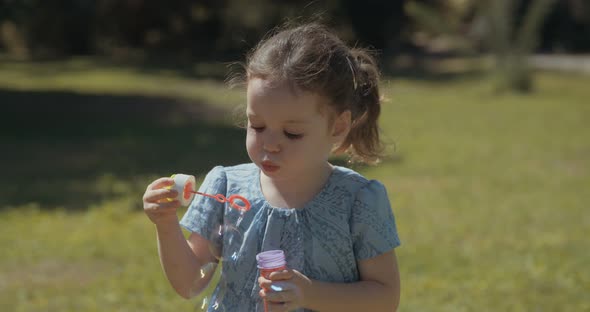 Slow motion of a little girl blowing soap bubbles outdoors