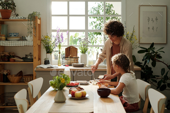 Young woman making sandwiches for youthful daughter and herself