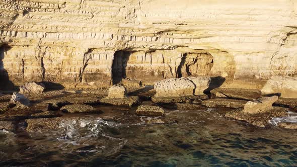 Flying Over Rocky Coastline Alongside Cliffside with Blue Mediterranean Sea Ocean Water Towards the