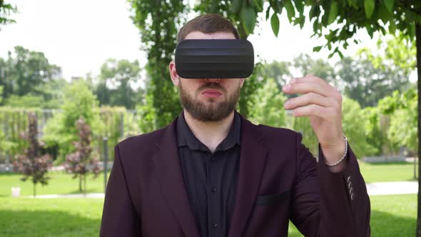 Man Businessman Wearing Virtual Reality Glasses in the Park Makes Hand Gestures