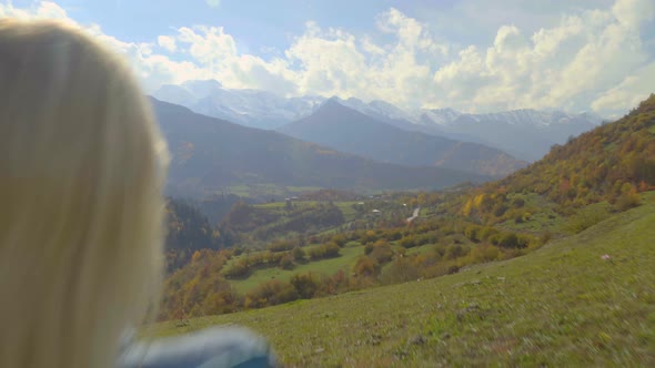 A woman sits on a chair and watches the mountain valley in autumn.