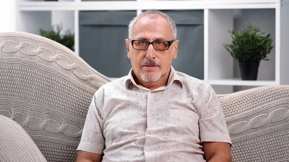 Portrait of Pensive Senior 70s Grandfather Posing on Comfy Couch