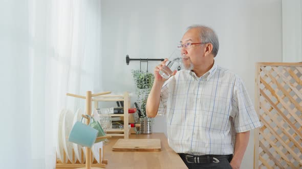 Asian senior mature male drinking a glass of water in kitchen at home