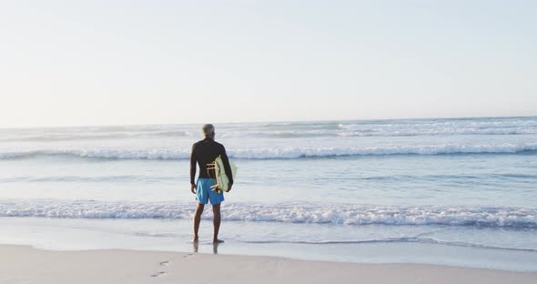 Senior african american man holding surfboard on sunny beach