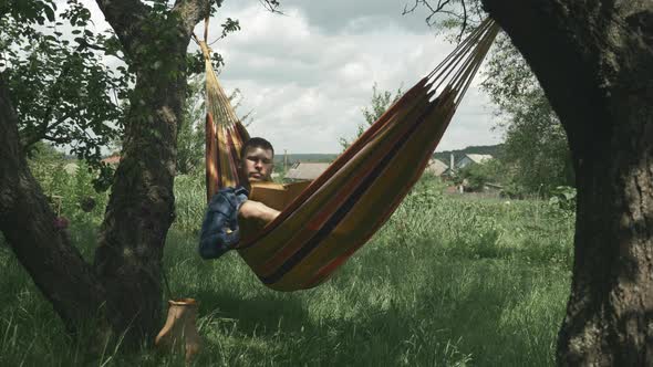 Relax in hammock. Camping. Man lying in hammock and reading book. Male relaxing in hammock