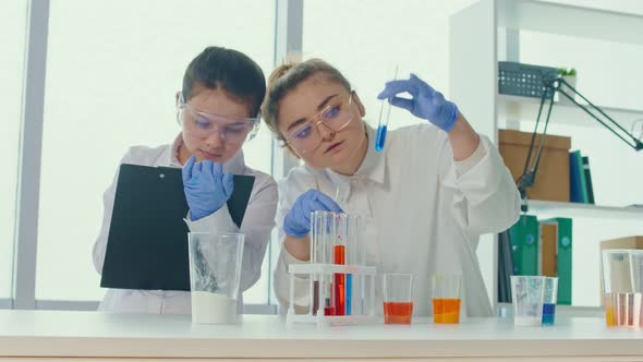 Girl With a Teacher in Lab Coats and Safety Glasses Conducts Experiments