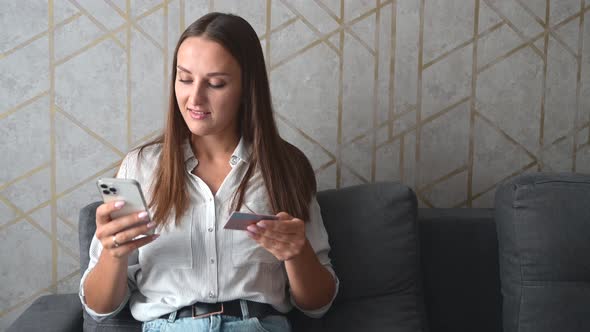 Smiling Young Woman Holds Smartphone and Debit Card Enjoying Online Shopping