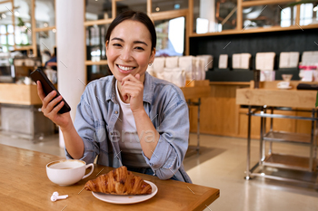t holding smartphone device using dating application on cellphone, laughing looking at camera, having fun sitting at cafe table enjoying coffee.