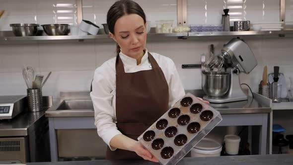A Female Pastry Chef Holds a Form for Making Praline Chocolates in a Kitchen