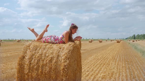 Girl Lying on Hay Ball on Summer Cultivated Field