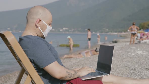 Man Freelancer in Medical Mask Work on Laptop By the Sea