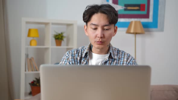 Young Asian Man Working Remotely on Laptop at Home Office