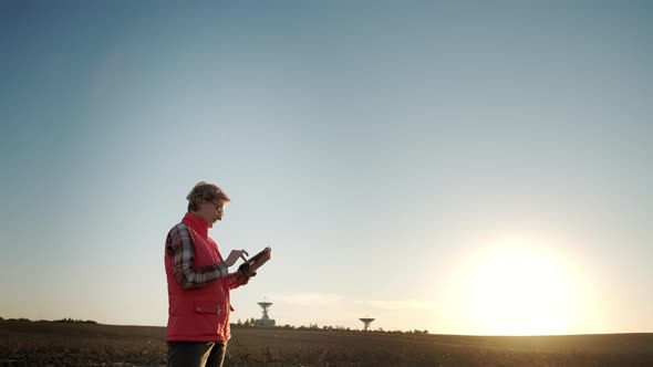 Against the Blue Sunset Sky of Farmer Woman Working with Tablet in Field Analyzes Quality of Crop