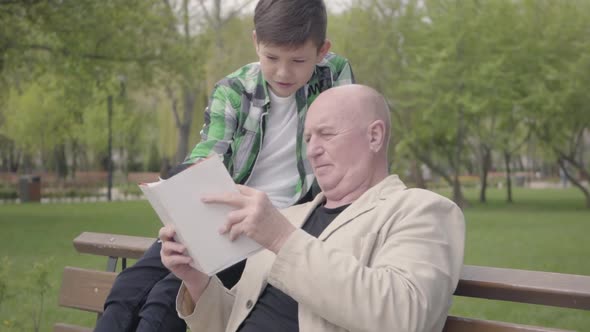 Portrait Cute Grandfather and Adorable Grandson Sitting in the Park on the Bench