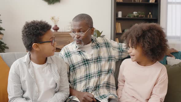 Two African American Kids Talking to Their Grandfather Sitting Together at Home on Christmas