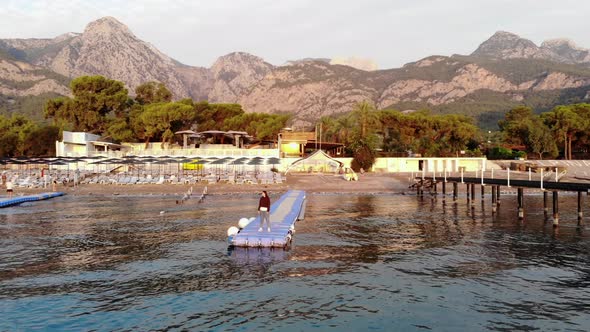 Shooting From Drone of a Young Girl Stands on a Plastic Modular Pontoon Among the Waves of the Sea