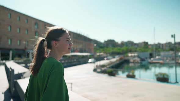 Pensive blonde woman wearing green t-shirt looking at view on the seafront near yachts