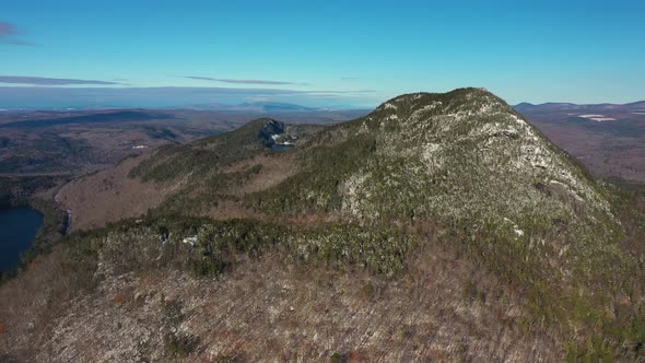 Aerial slide to the right past a far off snow dusted mountain in Maine