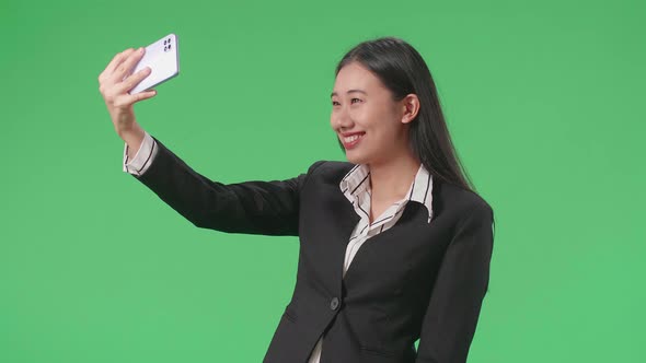 Asian Business Woman Making Selfie On Mobile Phone While Standing On Green Screen In The Studio