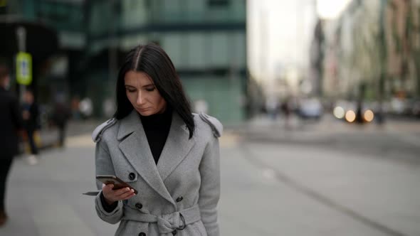 Middleaged Rich Lady is Walking in Business City Area Holding Modern Smartphone in Hands