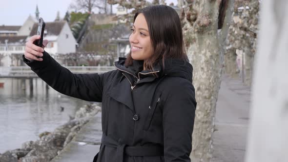 Young female model taking selfies on vacation in small wintry town on the bank of a river.