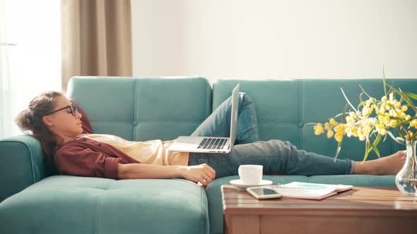 A Young Woman Lazy Working From Home While Lying on a Couch with a Laptop