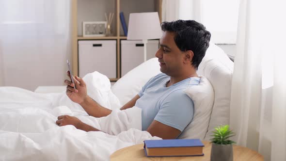 Happy Indian Man with Smartphone in Bed at Home