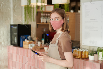 ring apron and protective mask starting workday in cafe holding digital tablet looking at camera