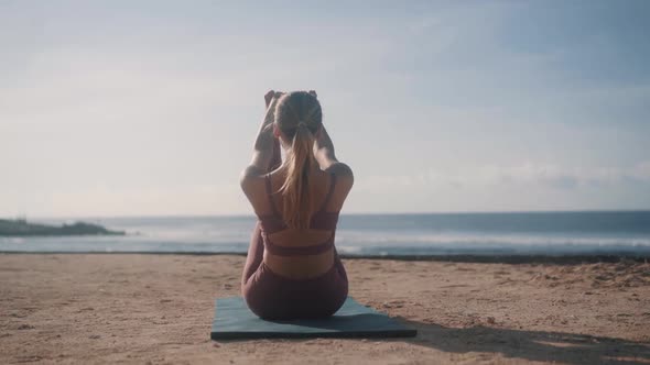 Girl Lifts Legs Stretching Body with Yoga Pose on Sand Beach